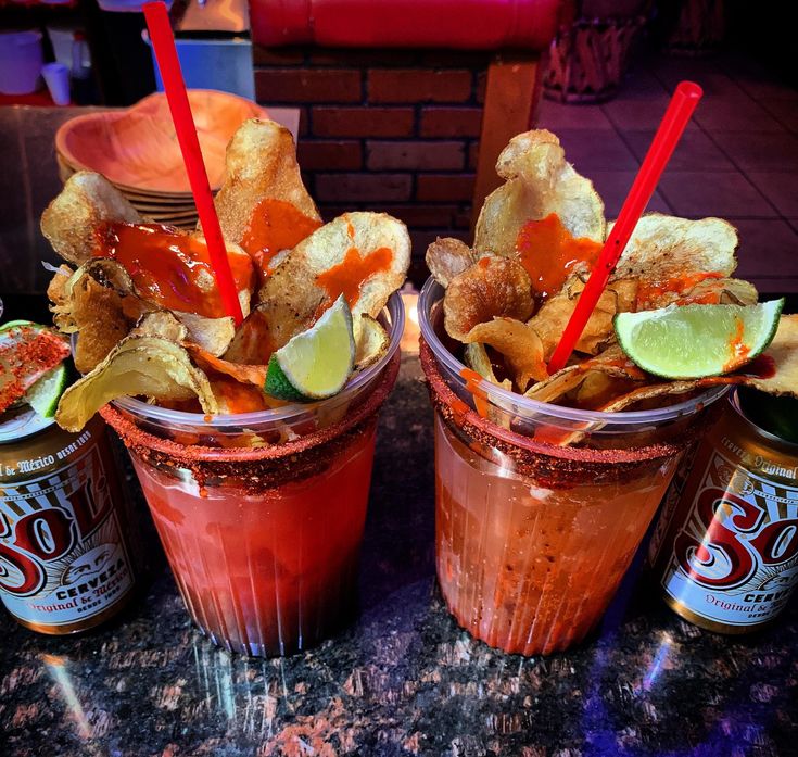 two cups filled with drinks and chips on top of a marble counter next to a brick wall