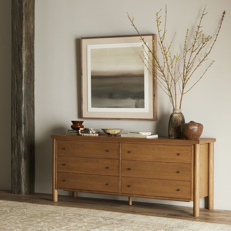 a wooden dresser sitting next to a painting and vases on top of each other