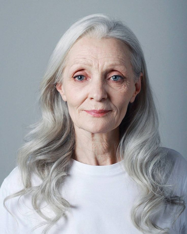 an older woman with grey hair and blue eyes wearing a white t - shirt looking at the camera