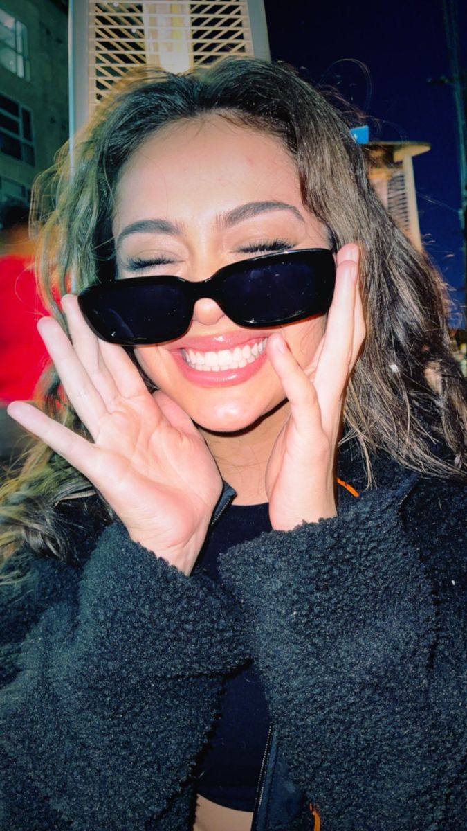 a woman with sunglasses on her face and hands to her face, smiling at the camera