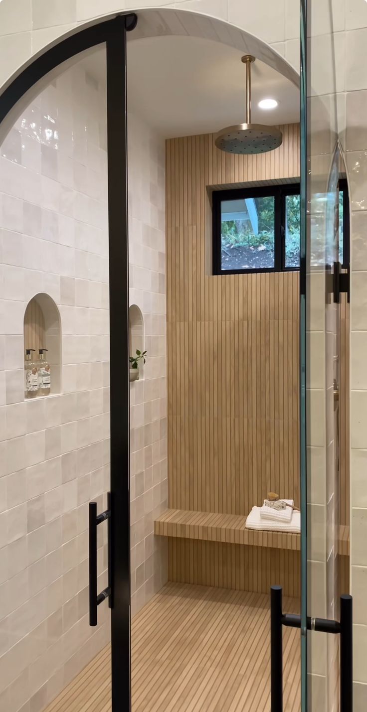 the inside of a bathroom with a wooden bench and glass shower door, in front of a window