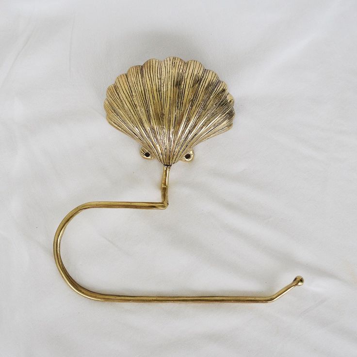 a gold towel ring with a shell on it's end and a hook in the middle