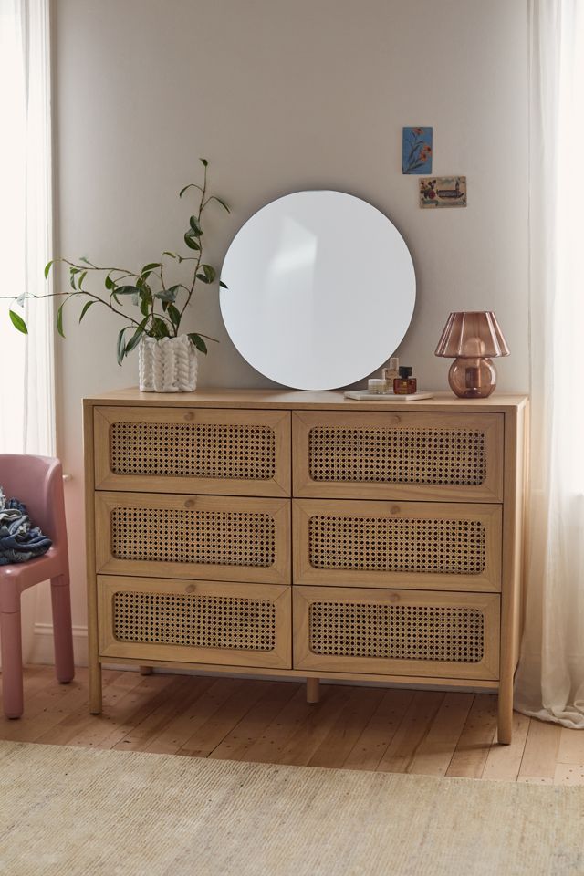 a wooden dresser with a mirror on top of it next to a pink chair and potted plant