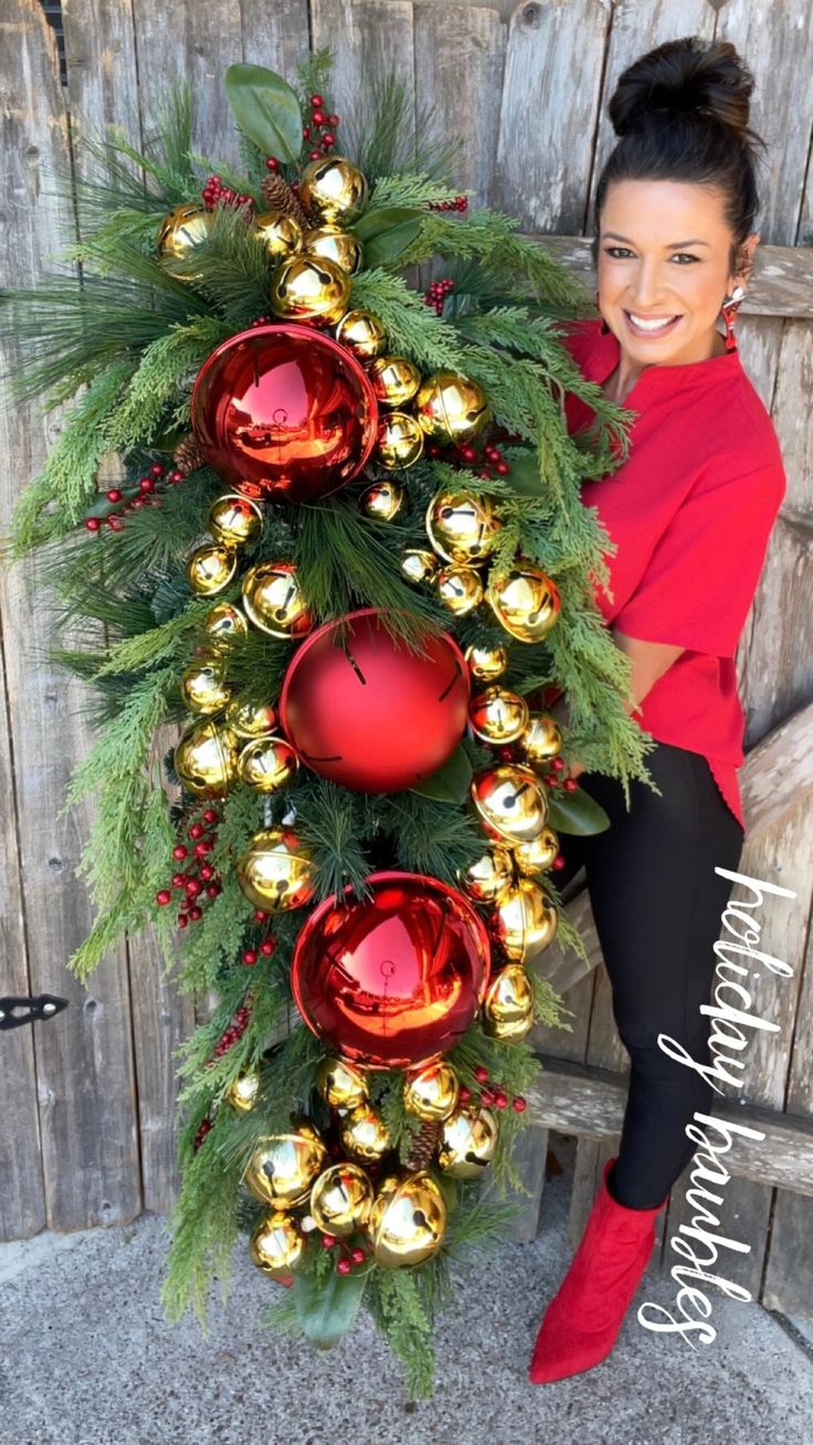 a woman sitting on a bench next to a christmas wreath with ornaments and greenery