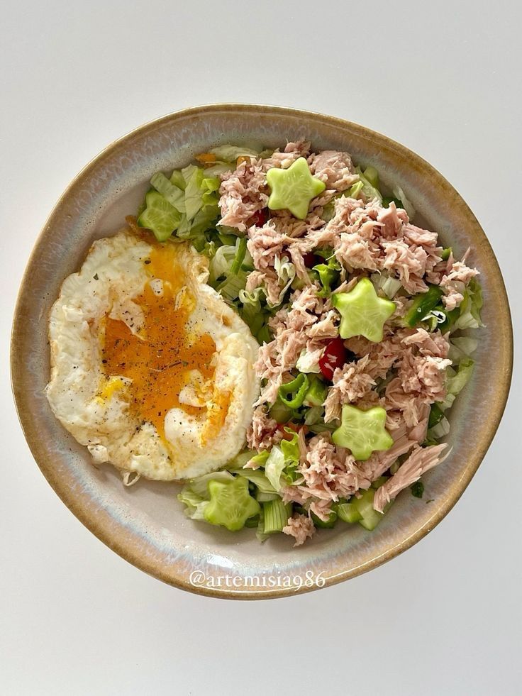 a salad with an egg on top and meat in the middle is sitting on a plate