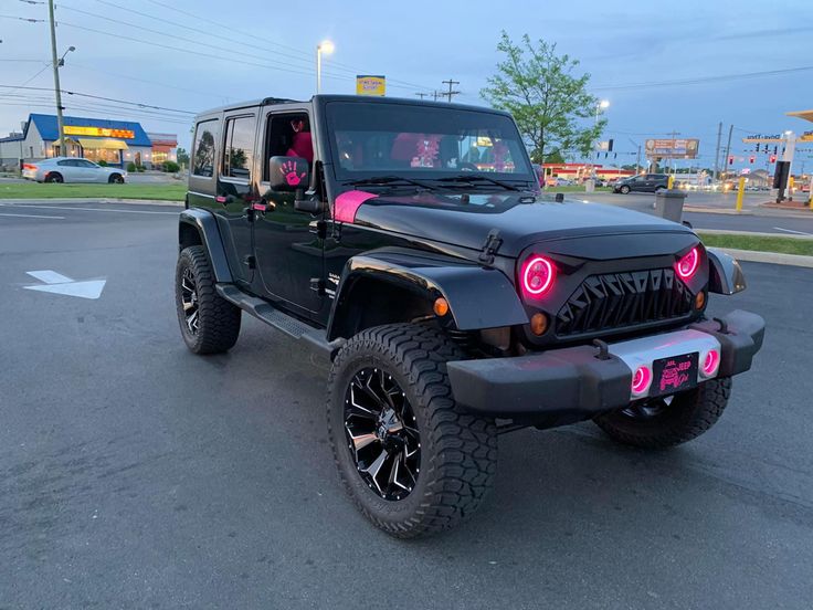 a black jeep with pink lights parked in a parking lot