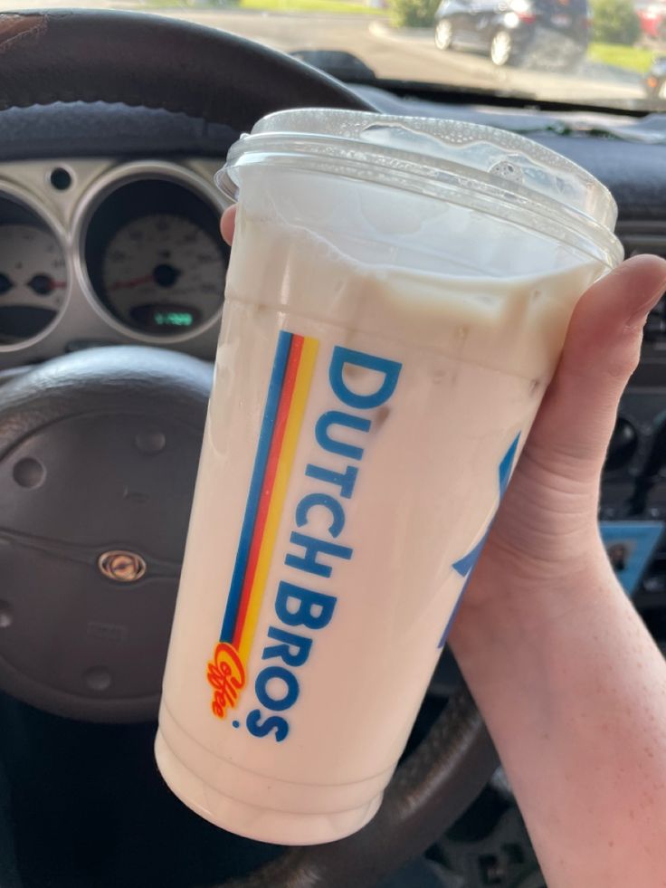 a person holding up a drink in the drivers seat of a car with steering wheel behind them