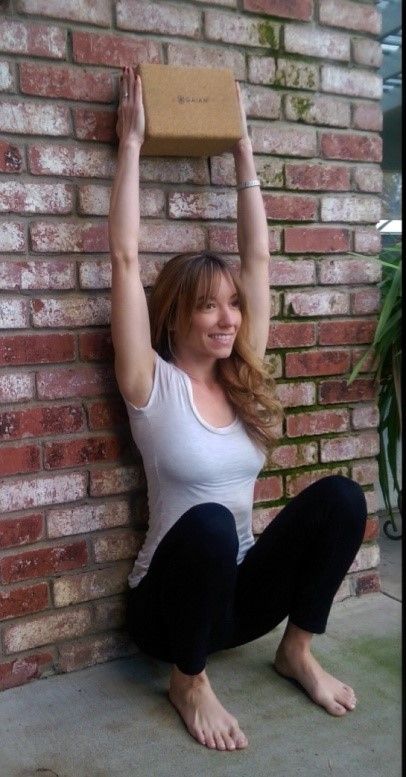 a woman sitting on the ground with her hands up in front of a brick wall