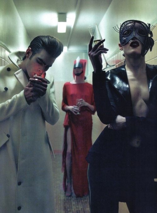 two men in masks are looking at their cell phones while another man stands near them