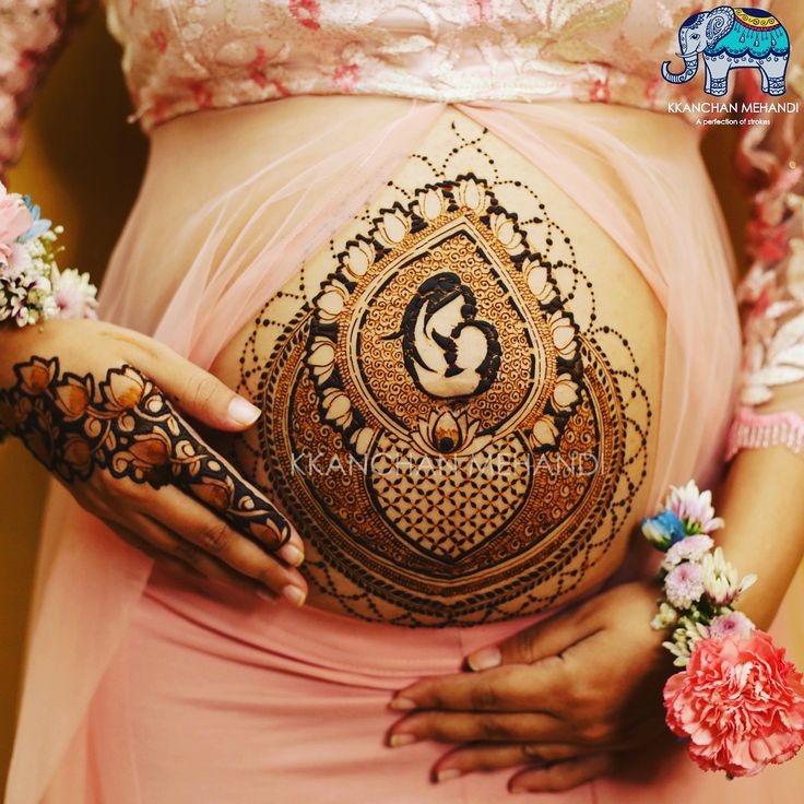 a pregnant woman's belly with henna tattoos on it and flowers in her hands