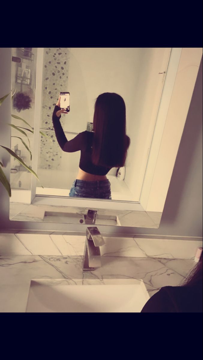 a woman taking a selfie in front of a bathroom mirror with her cell phone