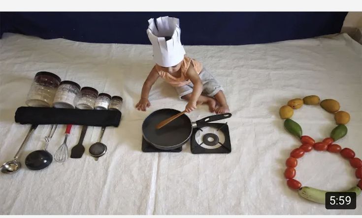 a baby is standing on top of a bed with food and utensils in front of it