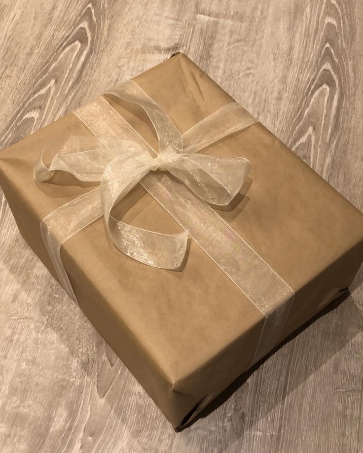 a brown box with a white ribbon on it sitting on a wooden floor next to a wall