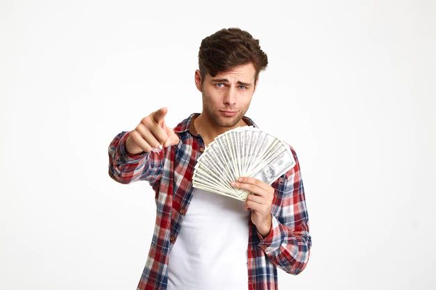 a young man is holding money and pointing at the camera with his finger while standing against a white background