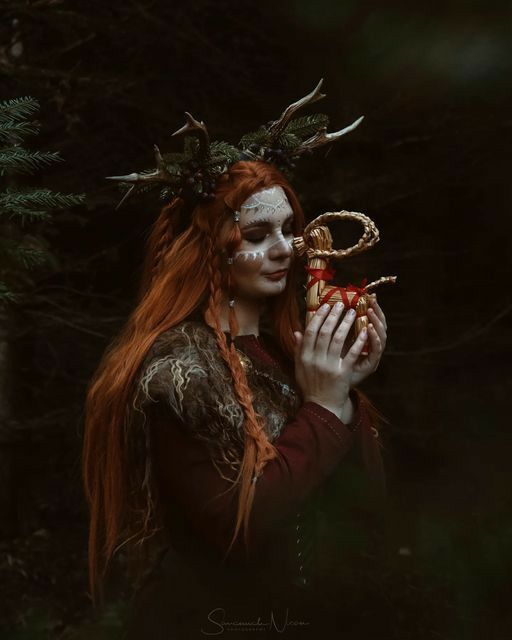 a woman with long red hair holding an apple in her hands and deer antlers on her head