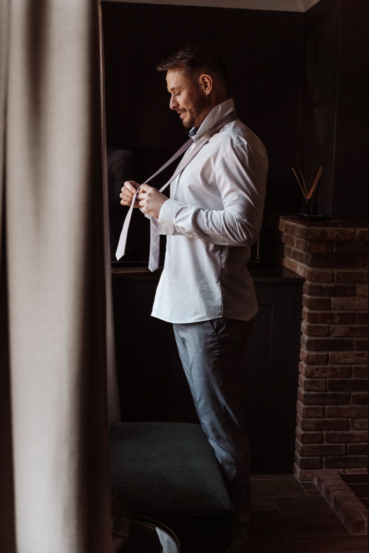 a man standing in front of a window tying his tie