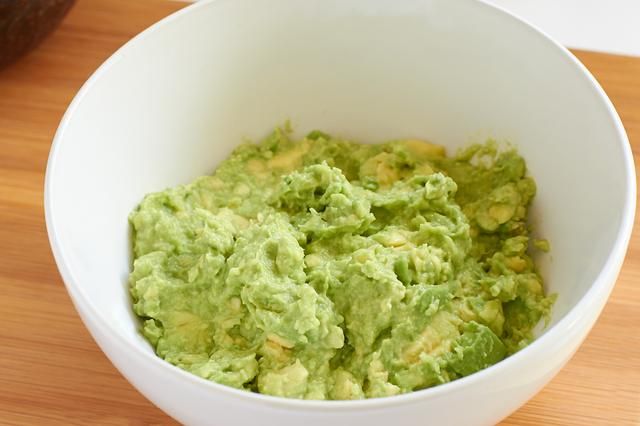 a white bowl filled with guacamole sitting on top of a wooden table