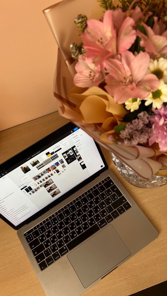 an open laptop computer sitting on top of a wooden desk next to a bouquet of flowers