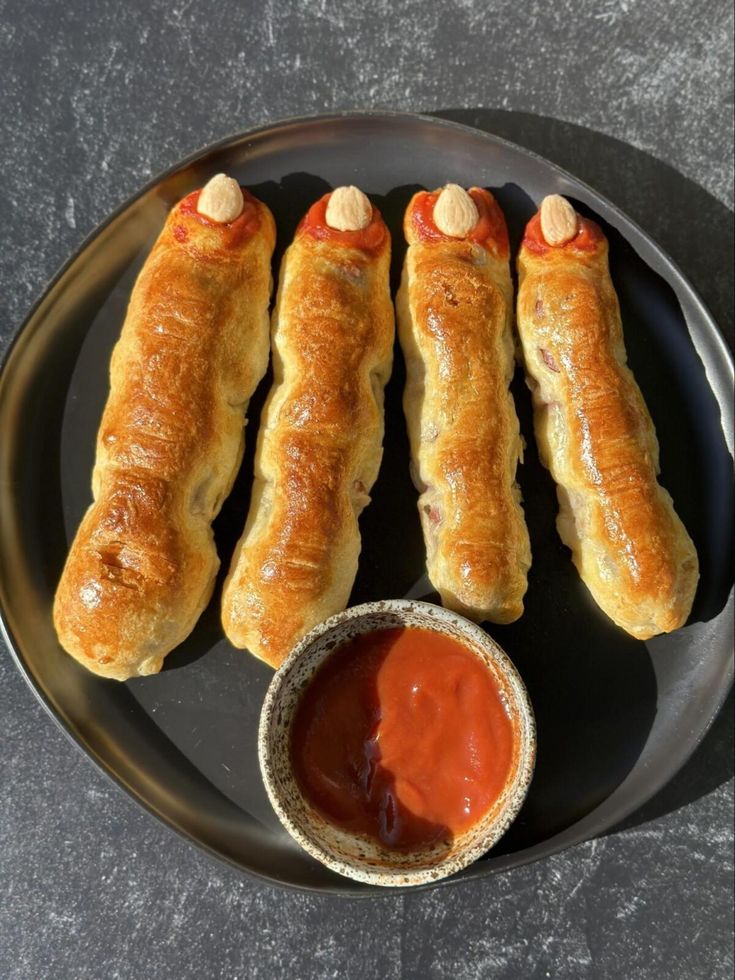 four sausages are on a plate with ketchup and mustard in a bowl