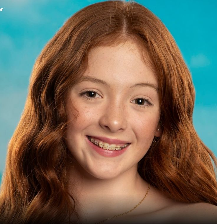 a woman with long red hair smiling at the camera and posing for a photo in front of a blue background