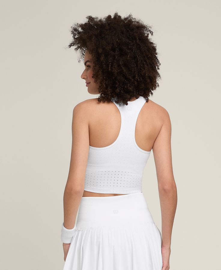 the back of a woman wearing a white tennis skirt and cropped tank top with cut outs