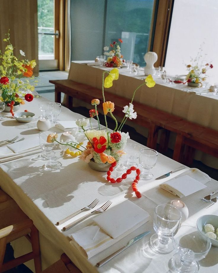 the table is set with flowers in vases and place settings for two people to sit at