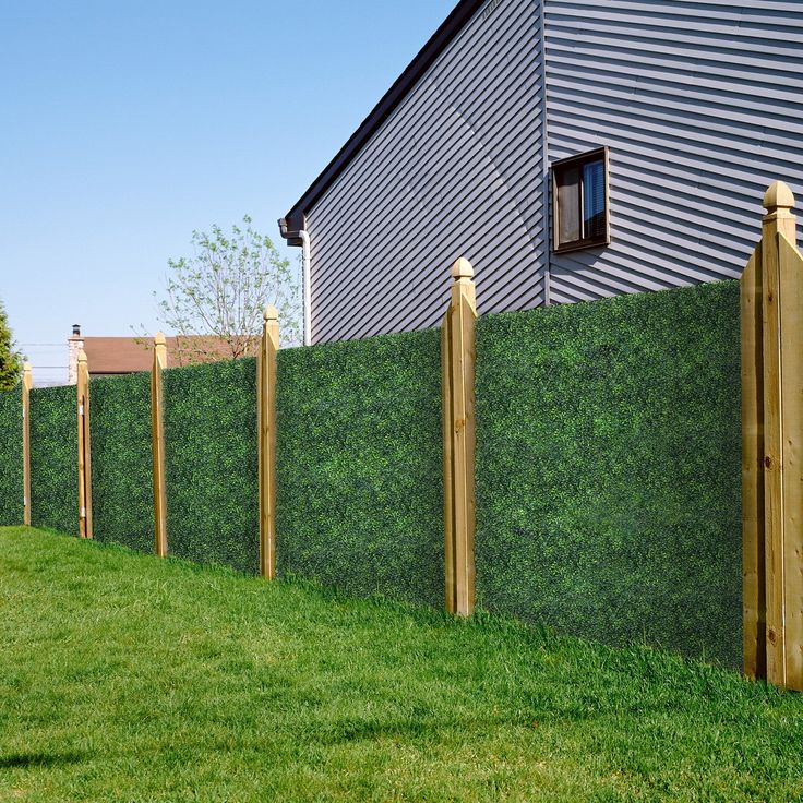 a green fence with wooden posts in front of a house and grass area next to it