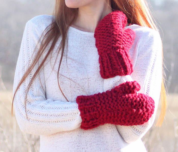 a woman wearing a red knitted mitt and scarf in front of a field