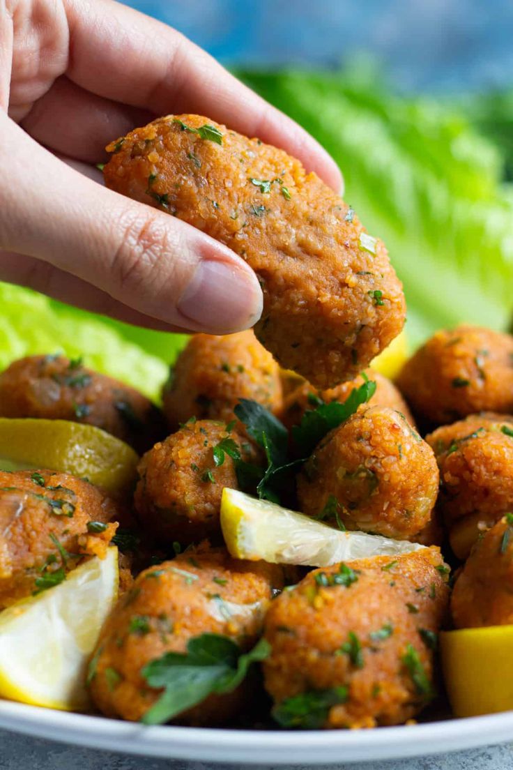 a person dipping some food into a bowl with lemon wedges and parsley on top