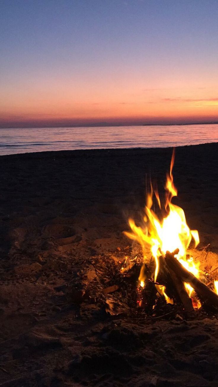 a campfire on the beach at sunset