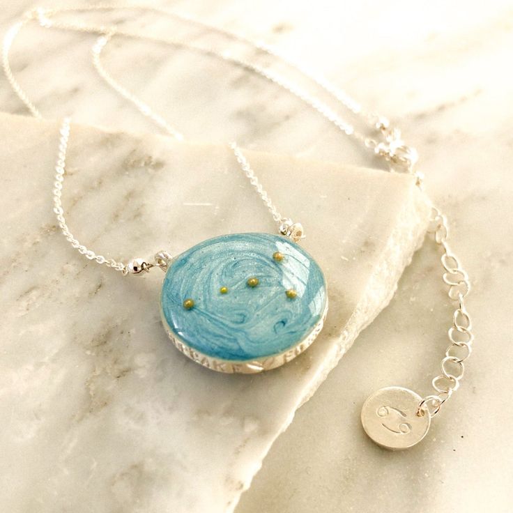 Image with a necklace placed on broken pieces of marble. Sterling silver necklace with sky blue background and the Cancer constellation made of gold beads. Custom stamping across the pendant reads “cupcake forever”. Jewelry tag with Cancer symbol is attached to the adjustable chain of the necklace Celestial Sterling Silver Necklace Gift, Celestial Sterling Silver Necklace For Gift, Celestial Sterling Silver Necklaces As A Gift, Celestial Sterling Silver Necklace With Adjustable Chain, Celestial Satellite Chain Jewelry As Gift, Celestial Jewelry With Satellite Chain For Gifts, Celestial Jewelry With Satellite Chain As A Gift, Celestial Style Jewelry With Satellite Chain As Gift, Blue Sterling Silver Cable Chain Jewelry