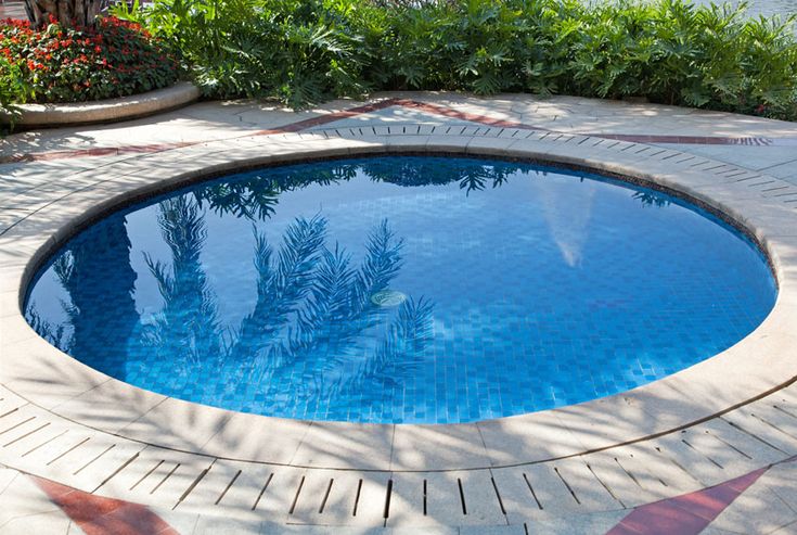 an empty swimming pool in the middle of a yard with trees and flowers around it