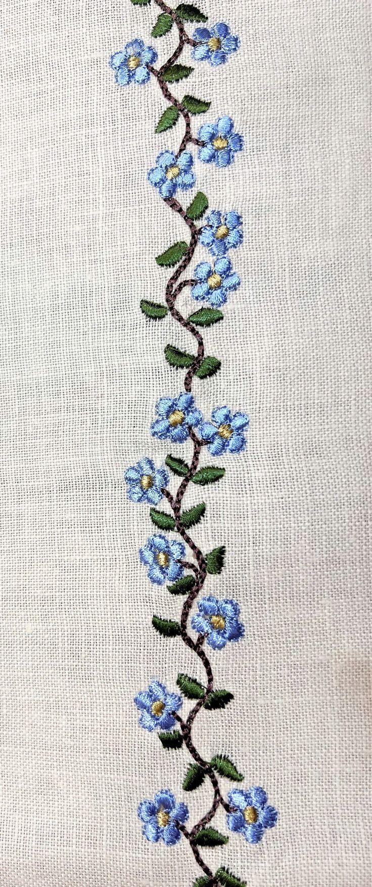 blue flowers are embroidered on the side of a white cloth with green leaves and stems