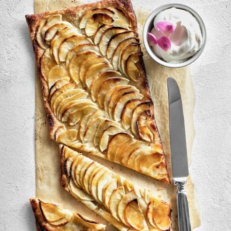 an apple tart with a knife and bowl of yogurt next to it