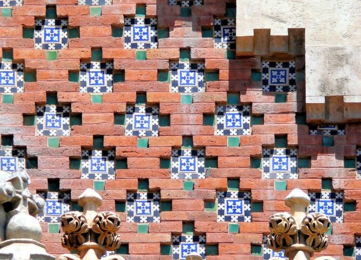 an intricately designed brick wall with blue and green tiles on the outside, along with decorative gargoyles