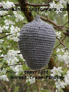 a crocheted beehive hanging from a tree with white flowers in the background