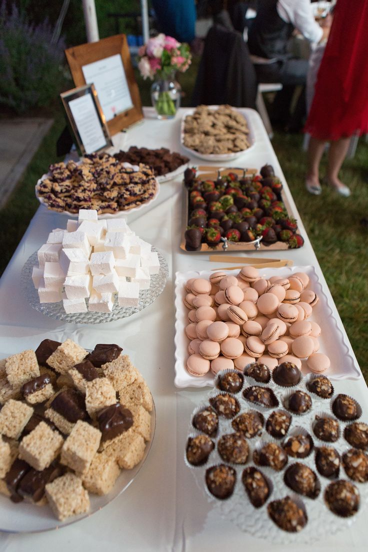 an assortment of desserts and sweets on a long table outdoors with people in the background