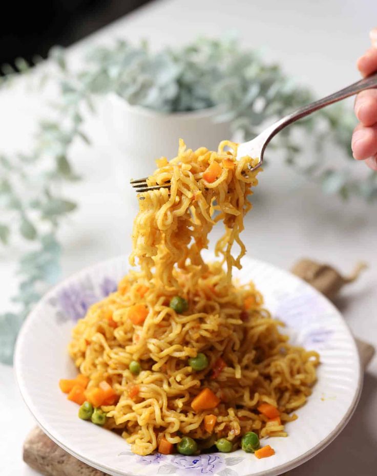 someone holding a fork full of noodles with peas, carrots and peas on it