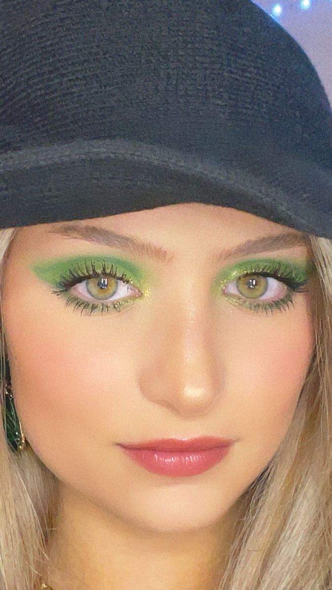 a woman with bright green makeup is wearing a black hat and has long blonde hair