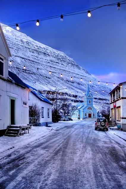 a small town street with snow on the ground and mountains in the background at dusk