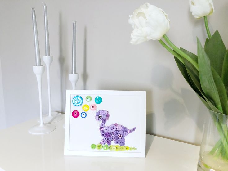 there is a card with a purple dinosaur on it next to some flowers and candles