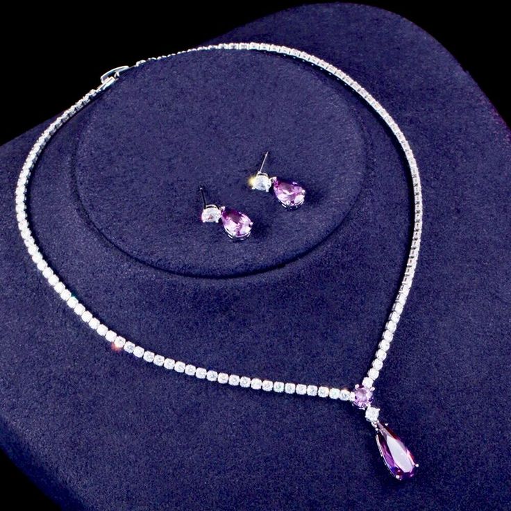 A beautiful two-piece bridal jewelry set with an incredible sparkle! Adorned with intricately faceted purple and clear cubic zirconia that capture the light from every angle with a perfectly translucent appeal, the pieces are platinum plated for a flawless finish which enhances the intricate detailing and conveys a modern take on old elegance. Necklace: 16.5" (approx. 42cm) long with a secure fold-over closure; pendant is 1" (approx. 2.5cm) long. If longer is needed please leave a note at checko Purple Diamond Necklace For Wedding, Purple Diamond Wedding Necklace, Purple Diamond Necklaces For Wedding, Dazzling Purple Jewelry With Diamond Accents, Purple Rhinestone Wedding Necklace, Purple Rhinestones Jewelry For Anniversary, Elegant Purple Cubic Zirconia Jewelry, Purple Rhinestone Jewelry For Anniversary, Purple Cubic Zirconia Jewelry Sets For Gift