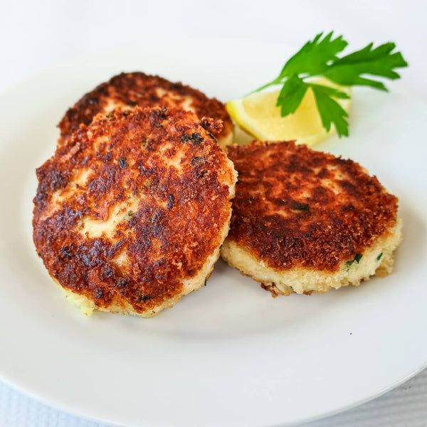 two crab cakes on a white plate with lemon wedges