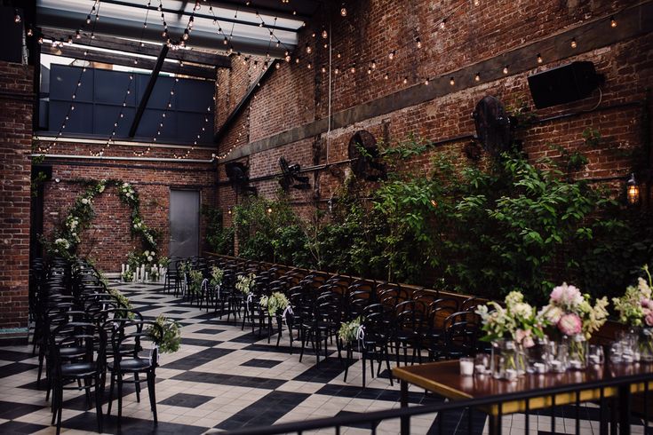 an indoor wedding venue with black and white checkered flooring, greenery and hanging lights