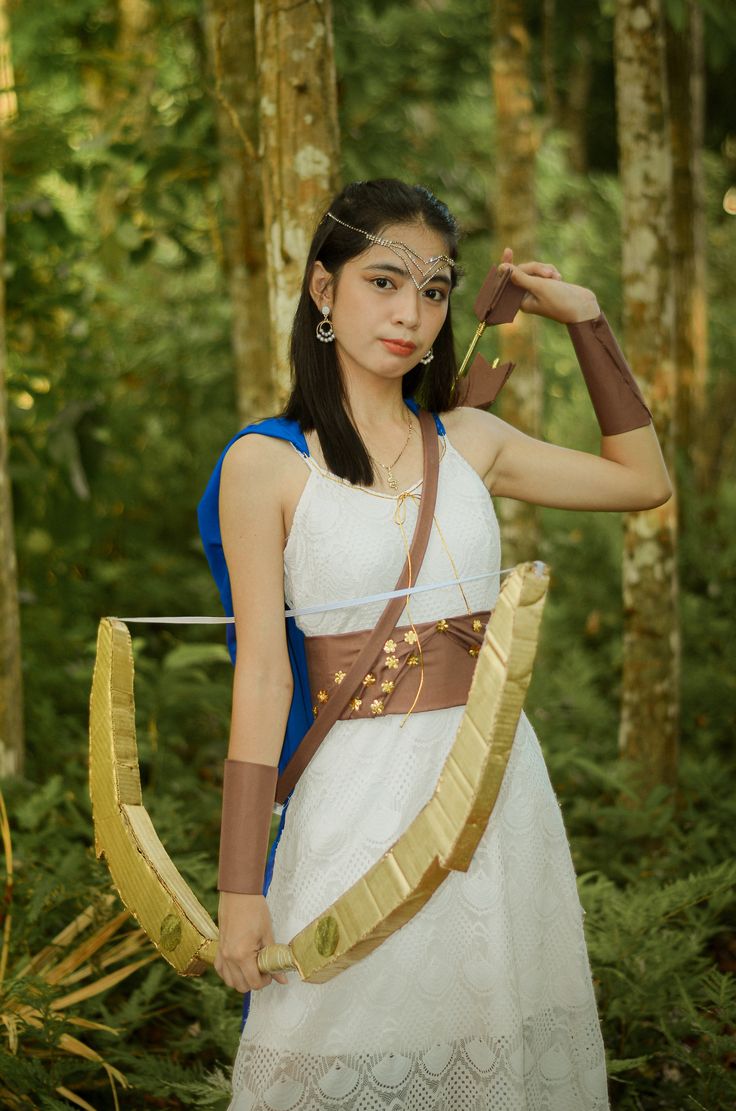 a woman dressed in costume holding an arrow and wearing a white dress with gold accents