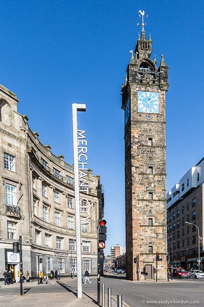 a tall clock tower sitting on the side of a road next to tall brick buildings