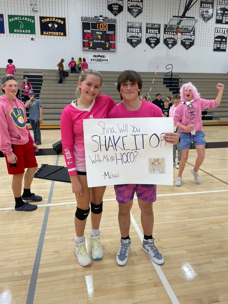 two girls in pink shirts holding up a sign that says shake it to what's hoo?