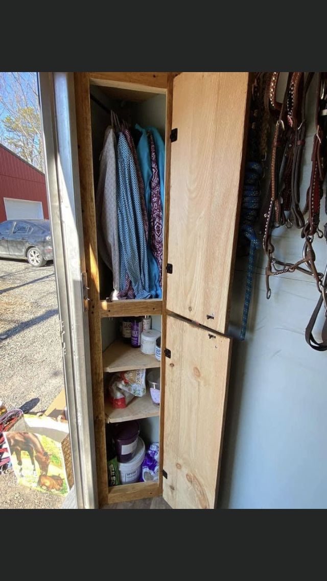 an open wooden cabinet sitting inside of a room next to a horse shoe rack and other items