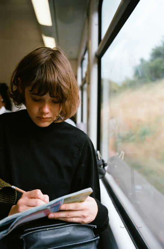 a woman sitting on a train looking at her cell phone while holding a book in her hand