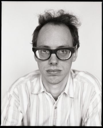 black and white photograph of a man with glasses looking at the camera while wearing a striped shirt